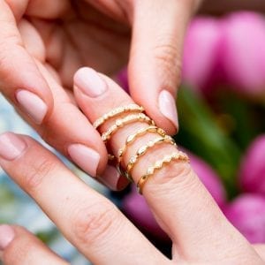 woman stacking 5 gold and diamond rings on finger over pink and blue flowers