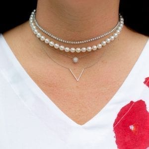 closeup of woman wearing pearl choker necklace and three white gold diamond necklaces layered on neck
