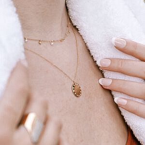 woman wearing two necklaces and a towel around her neck. rings on fingers