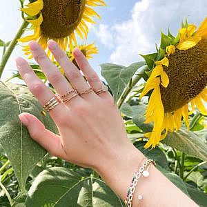 gold and diamond collection rings on women's hand with sunflowers